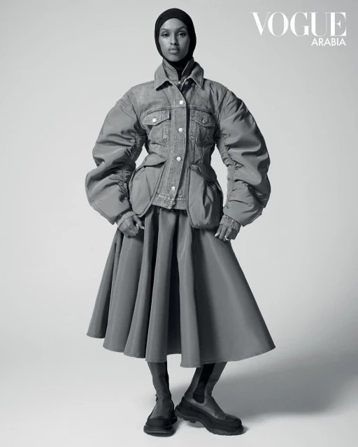 Editorial fashion shot of a woman in a denim jacket and skirt, accessorized with a black headscarf and boots, against a plain backdrop.