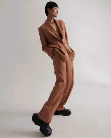 Model in a brown suit and thick-soled black shoes posing against a white background by Louis Christopher.