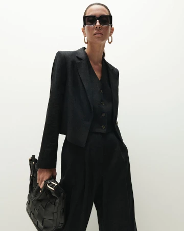Model in black suit wearing sunglasses and holding a woven bag against a bright white background