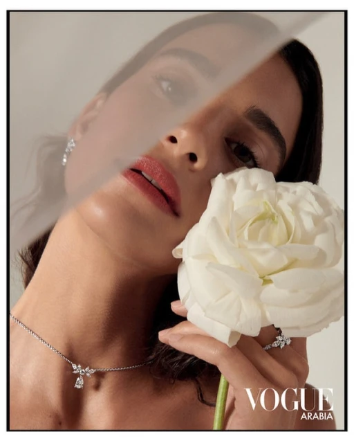 Woman with jewelry holds flower in a beauty style photograph. The light is soft and the background is blurred.