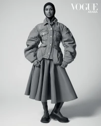 Model in quilted denim jacket and pleated skirt wearing a black hijab against a white seamless background