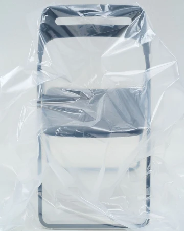 Still life of a dark grey folding chair partially covered in a clear plastic sheet, studio lit against a white background.