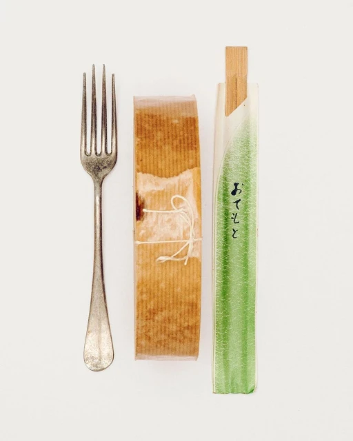 Still life flat lay composition of a silver fork, a wrapped pastry, and packaged chopsticks on a white background in vertical format.