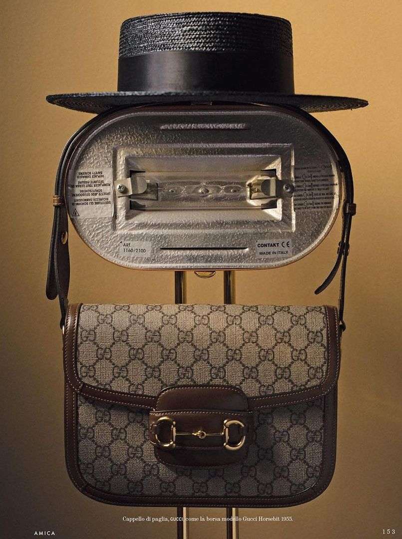 Fashion still life featuring a black straw hat, a silver vintage appliance, and a Gucci handbag, displayed in a studio setting.