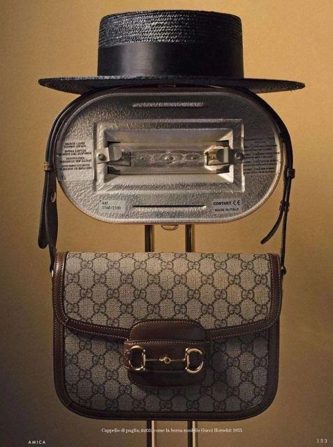Fashion still life featuring a black straw hat, a silver vintage appliance, and a Gucci handbag, displayed in a studio setting.
