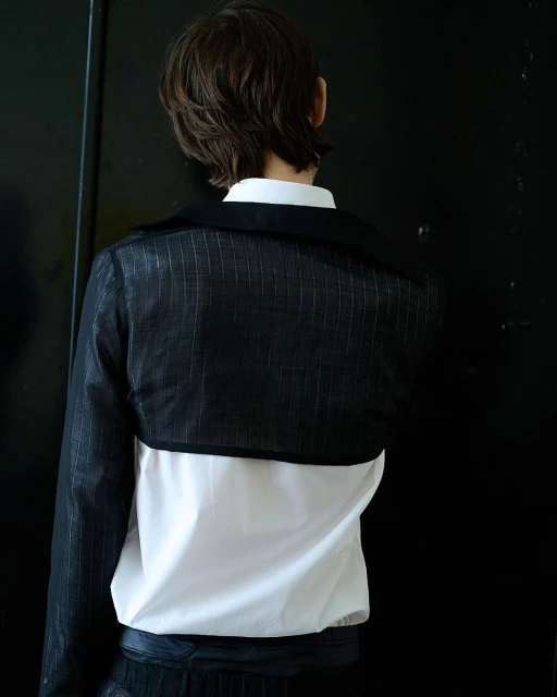 Back view of a person in a black and white outfit standing against a black background in an indoor environment, fashion photography.
