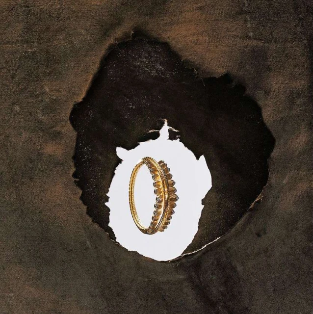 Gold bangle with decorative accents is showcased through a dark brown paper tear, highlighted against a bright white backdrop.