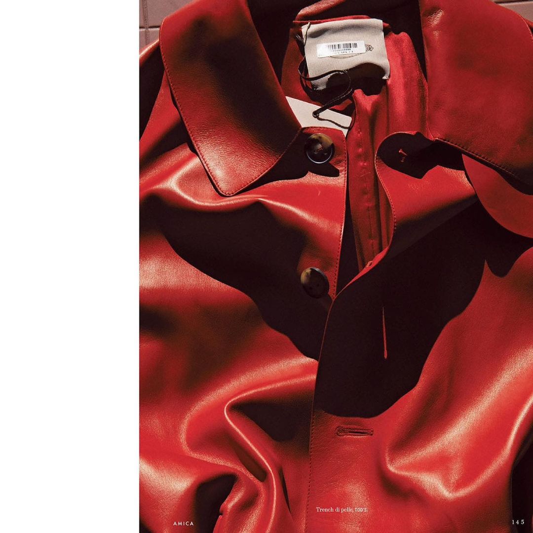 Close-up of a vibrant red leather trench coat with visible buttons and collar, showcasing fashion and texture, and high-contrast lighting.
