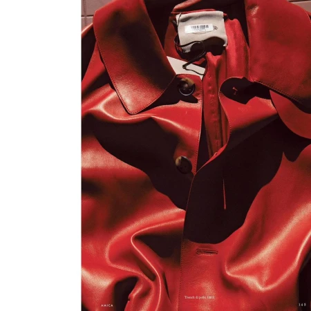 Close-up of a vibrant red leather trench coat with visible buttons and collar, showcasing fashion and texture, and high-contrast lighting.