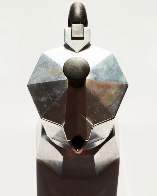 Close-up shot of a metal stovetop espresso maker, highlighting its geometric shape, metallic texture, and the simplicity of the design.
