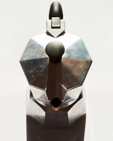 Close-up shot of a metal stovetop espresso maker, highlighting its geometric shape, metallic texture, and the simplicity of the design.