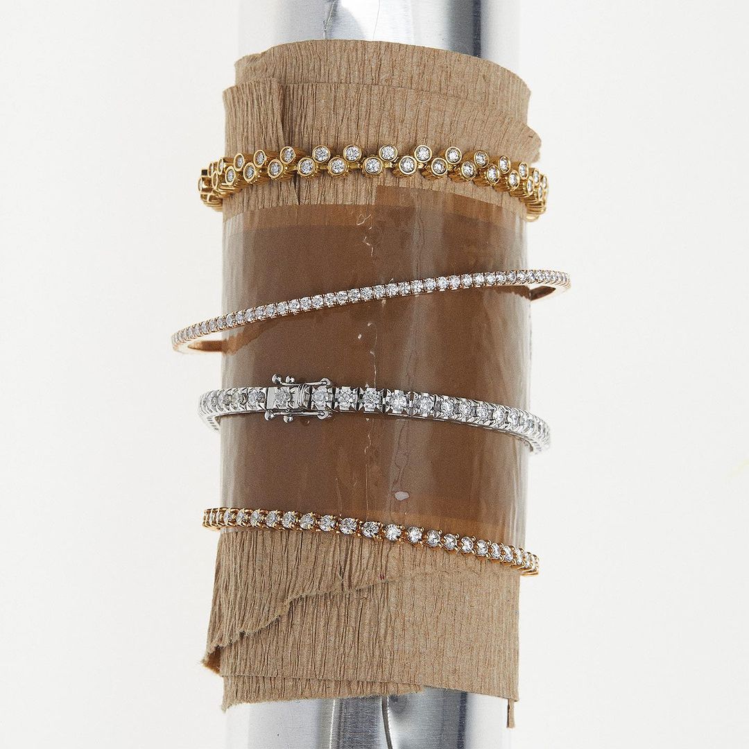 A collection of diamond bracelets in gold and silver tones are elegantly displayed on a cylindrical display, set against a bright backdrop.