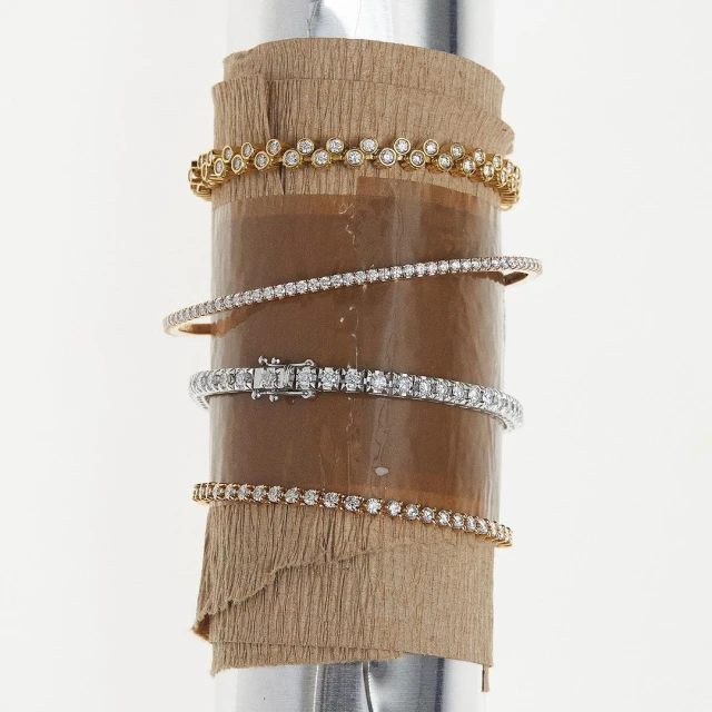 A collection of diamond bracelets in gold and silver tones are elegantly displayed on a cylindrical display, set against a bright backdrop.
