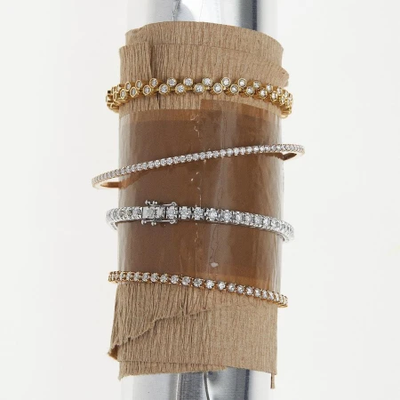 A collection of diamond bracelets in gold and silver tones are elegantly displayed on a cylindrical display, set against a bright backdrop.