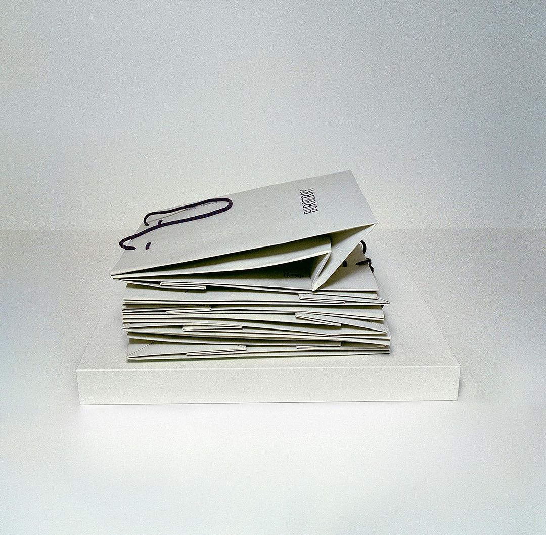 Stack of Burberry branded shopping bags in neutral tones against a white background. Fashion brand marketing still life image.