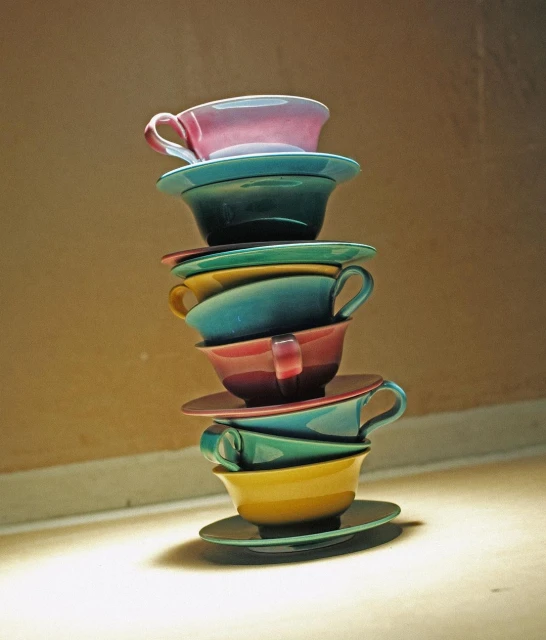 Stacked teacups in pink, green, yellow, and teal colors against a neutral background with soft light create a visually appealing composition.