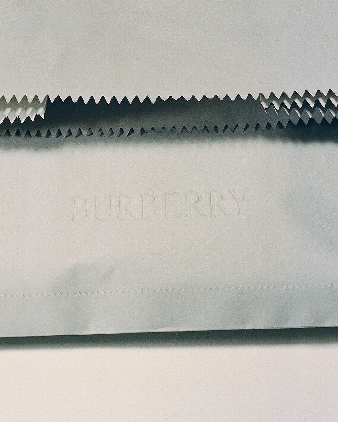 Minimalist shot of textured Burberry paper with jagged edges, showcasing the brand's name embossed on the surface and paper art.