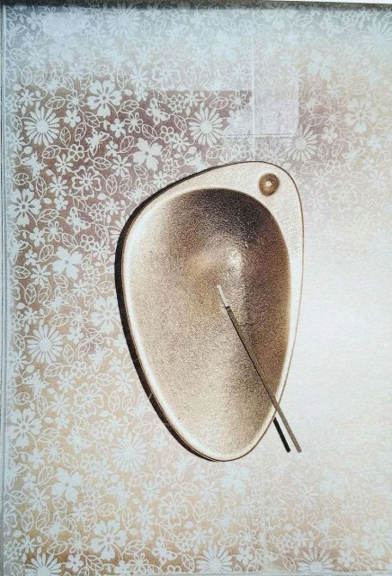 Abstract surreal art featuring a gold metallic bowl on a silver background with white floral patterns and two thin sticks.