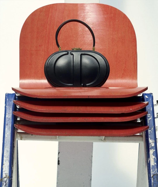 Black purse on a stack of coral chairs. A stylish studio shot of a black leather purse with gold hardware and a black handle.