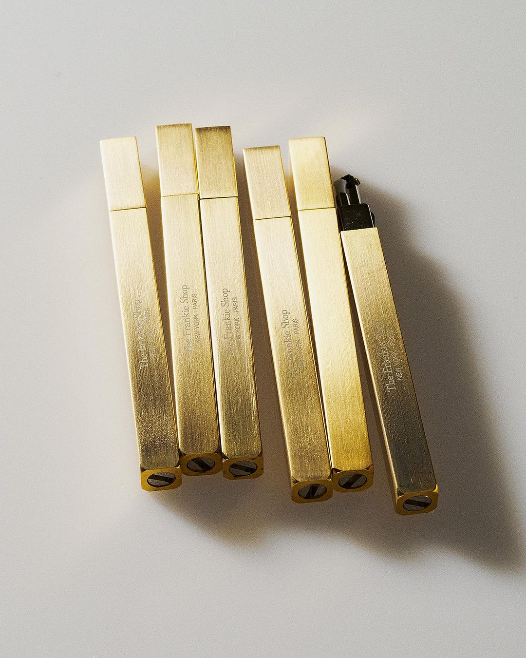 Several rectangular, golden-colored metal objects with text, arranged on a white surface in a studio setting.