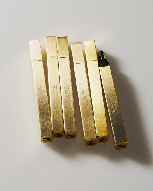 Several rectangular, golden-colored metal objects with text, arranged on a white surface in a studio setting.