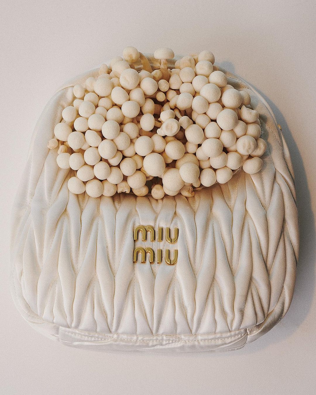 Miu Miu quilted white handbag with clustered white spherical elements, showcased on a plain background in a studio setting.