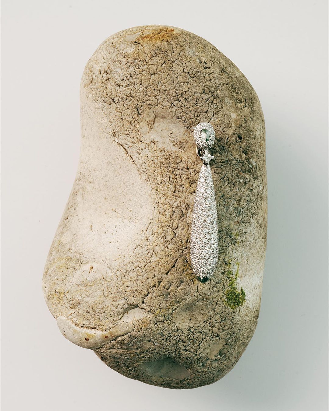 Elegant teardrop earring featuring sparkling gems on a textured rock against a plain background. Jewellery and natural elements.