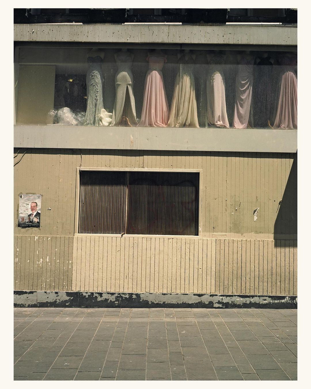 Exterior shot of an urban building showcasing a display of draped dresses behind glass windows, creating a surreal and artistic scene.