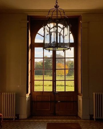 Interior view through a window, showcasing the light fixture, architectural details, and a vibrant landscape of trees and sky beyond.
