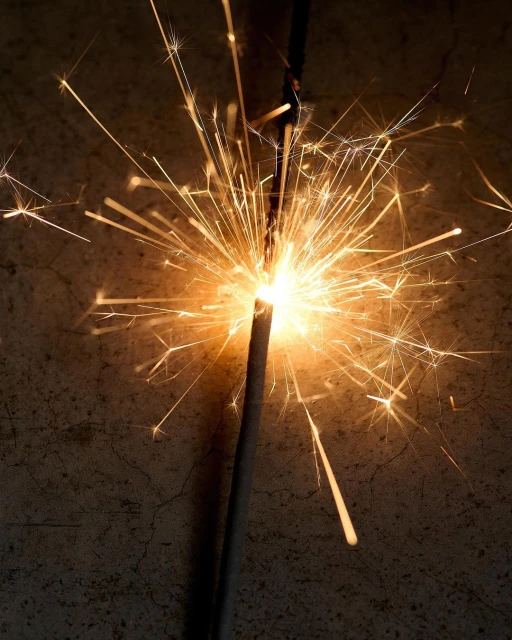 Close-up of a brightly lit sparkler emitting golden sparks against a dark, textured background, creating a festive and celebratory mood.