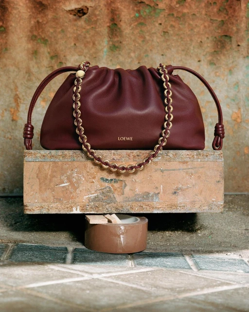 Burgundy Loewe Noto bag on a weathered surface with tiled floor, gold chain detail, and subtle logo for a fashion-forward look.