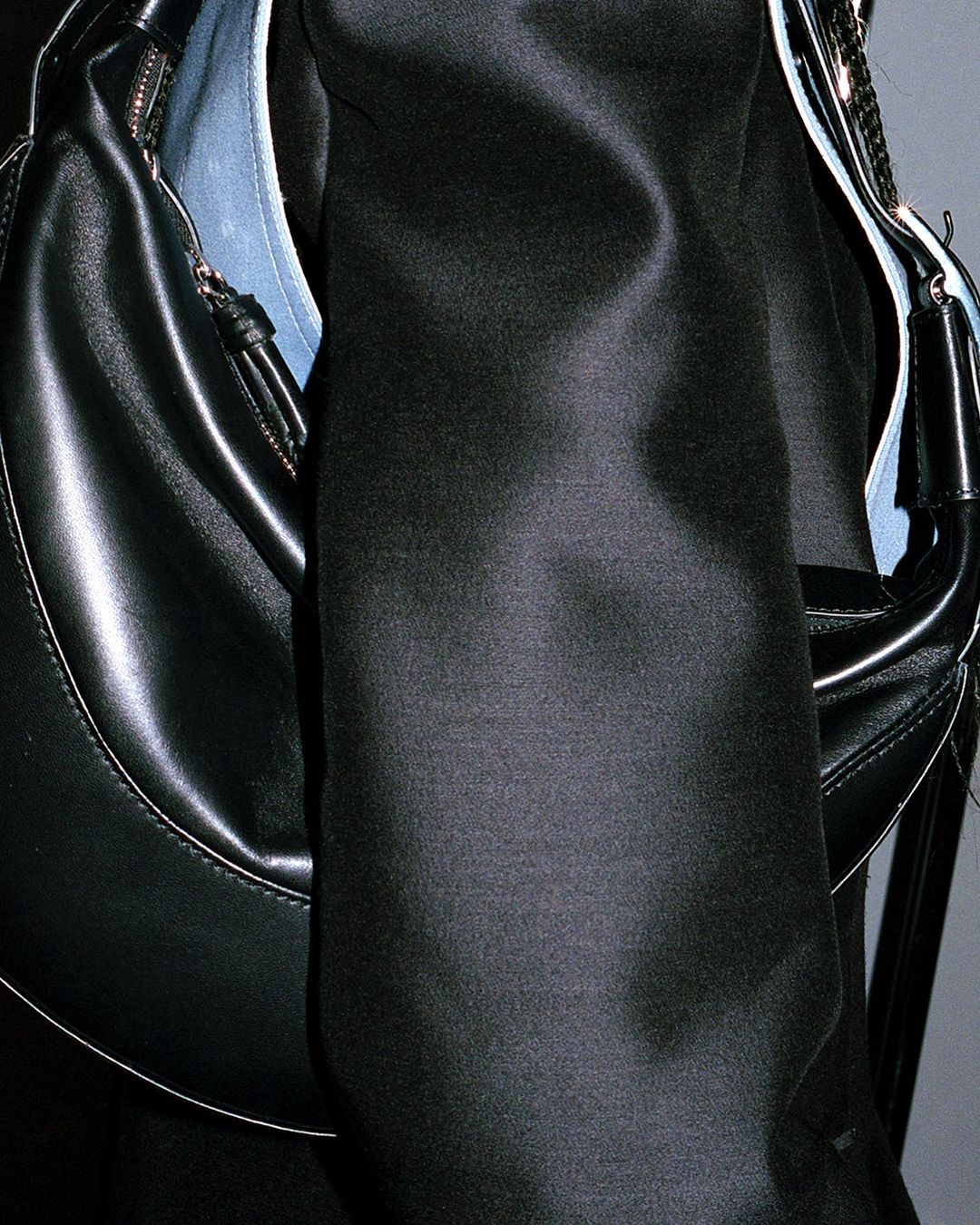 Close-up shot of a black crescent hobo bag made of shiny leather or pleather, with a black shirt, providing a fashion aesthetic.