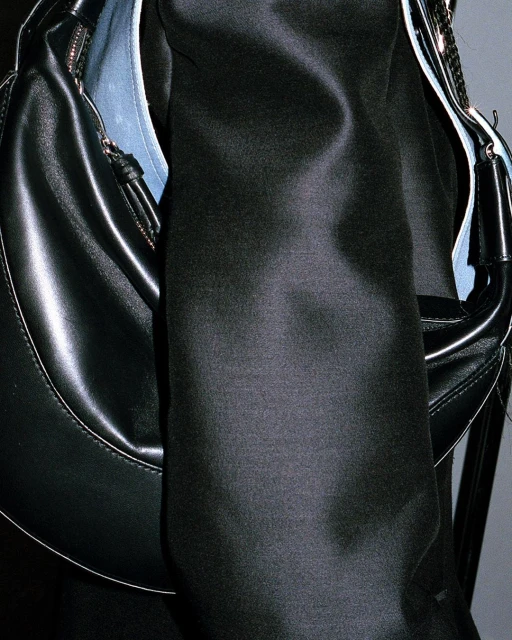 Close-up shot of a black crescent hobo bag made of shiny leather or pleather, with a black shirt, providing a fashion aesthetic.