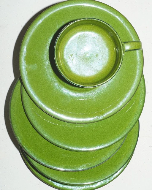 Overhead shot of a stack of green ceramic plates with a matching cup nestled on top, creating a visually appealing kitchenware still life.
