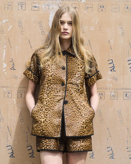 Fashionable young adult woman poses in a leopard print short set against a textured cardboard background. Studio fashion portrait.