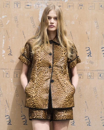 Fashionable young adult woman poses in a leopard print short set against a textured cardboard background. Studio fashion portrait.