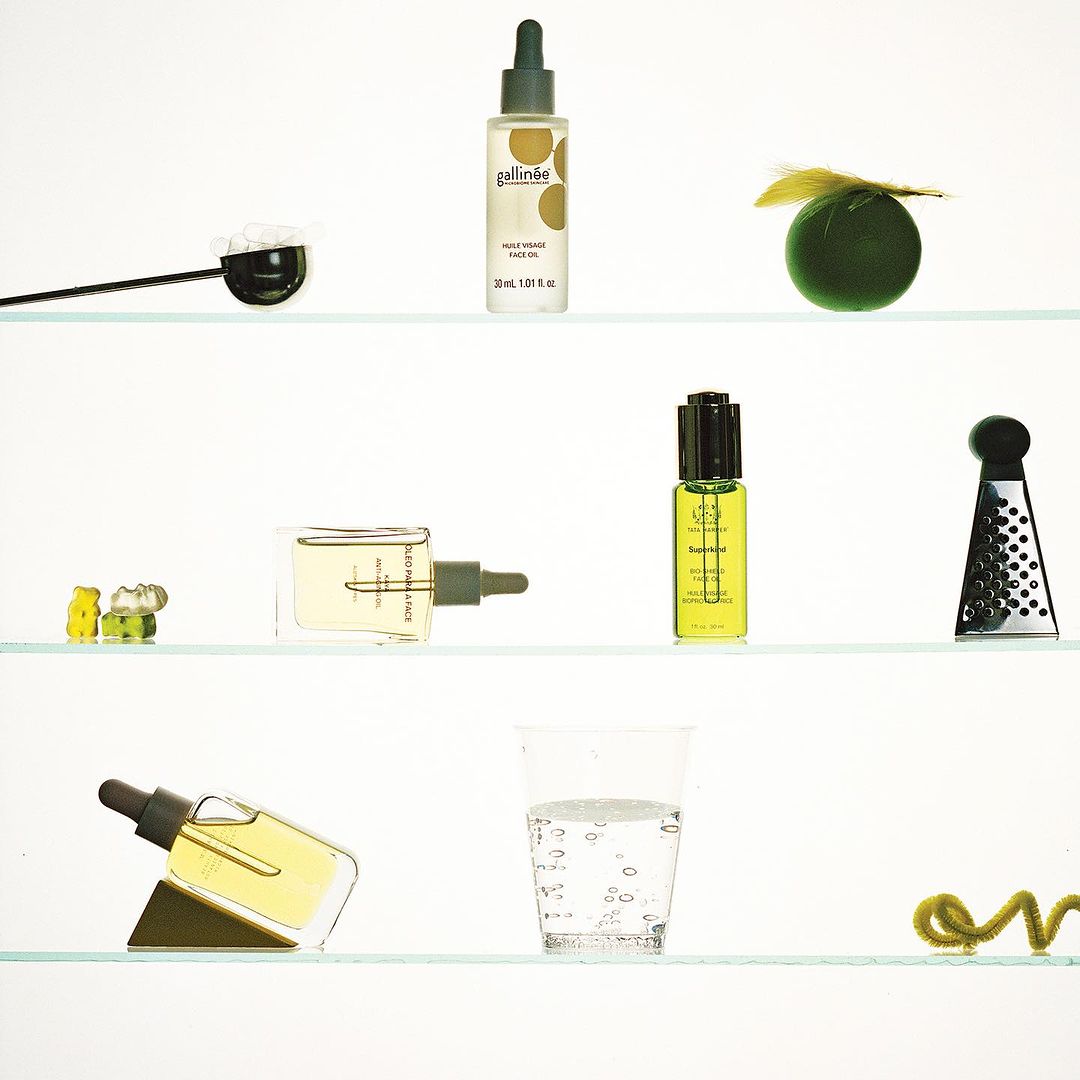 Botanical beauty product arrangement on shelves featuring skincare oil bottles, glass of water, and abstract decorative elements.