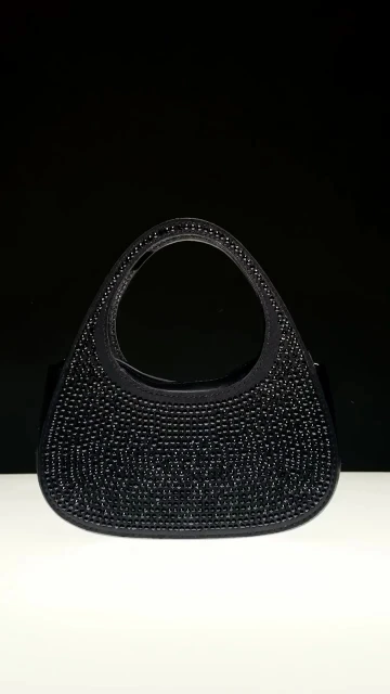 Elegant black beaded evening bag with a rounded shape and short handle, set against a gradient of black and white background.