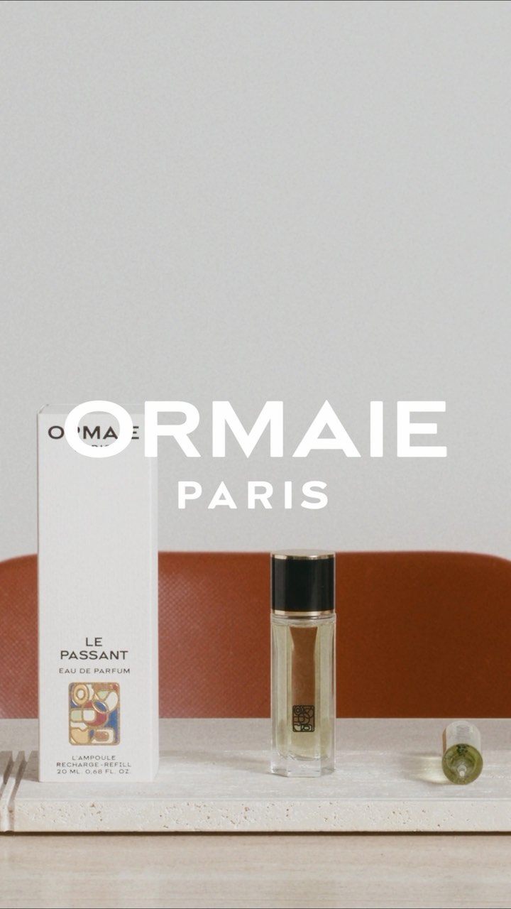 ORMIAIE Paris perfume bottle and packaging on a light marble surface with a muted orange background, product photography.