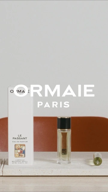 ORMIAIE Paris perfume bottle and packaging on a light marble surface with a muted orange background, product photography.