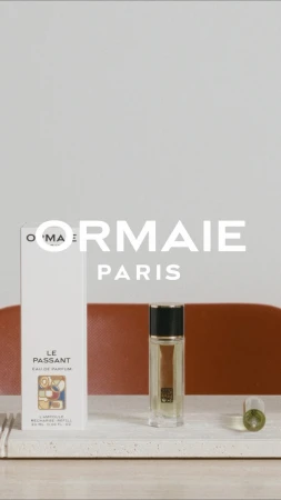 ORMIAIE Paris perfume bottle and packaging on a light marble surface with a muted orange background, product photography.