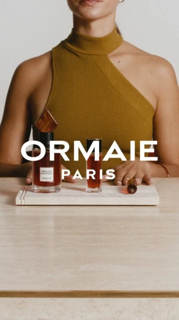 Beauty shot of perfume bottles on a marble tray with a model in an asymmetrical top with a neutral background, promoting fragrance products.