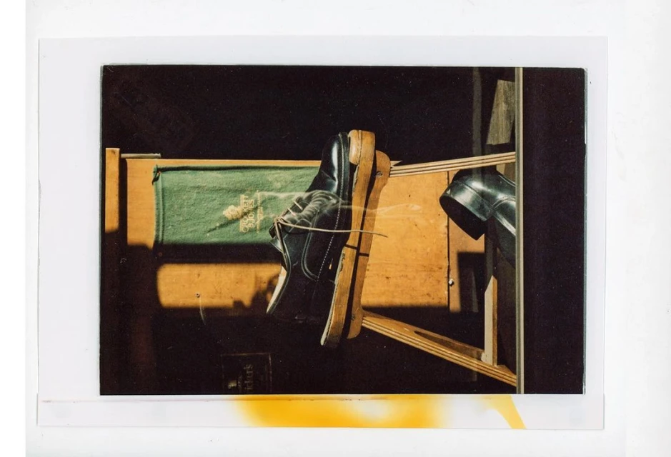 High-angle shot of two black dress shoes suspended between wooden structures, in a dimly lit room, creating a surreal, artful composition.