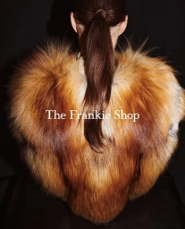 Model from behind wearing a textured faux fur jacket with brown hair tied in a ponytail against a solid black background.