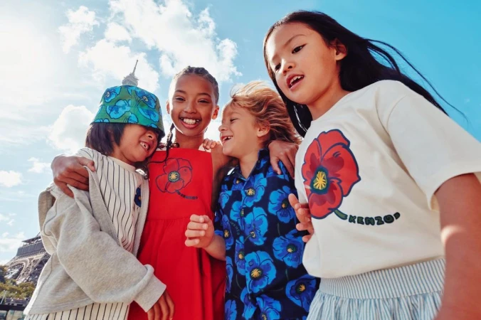Four children smiling together in front of the Eiffel Tower in Paris, wearing shirts and a hat with a matching floral pattern.