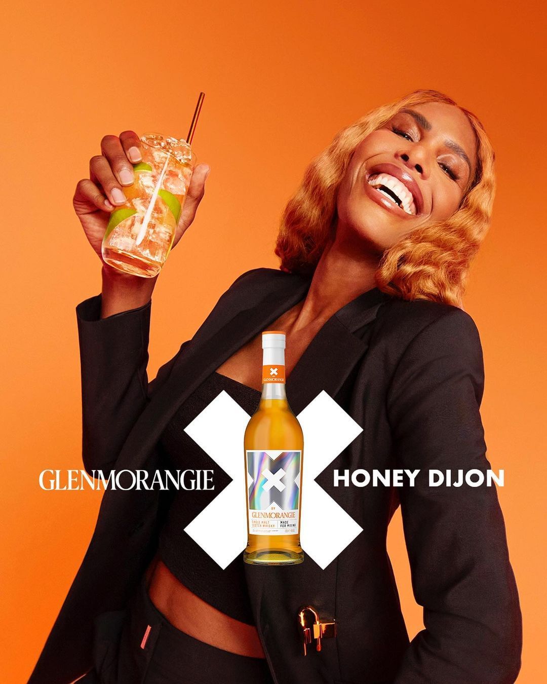 Woman smiling, holding a cocktail with a bottle of Glenmorangie Honey Dijon. Fashion, beauty, and beverage meet in a studio shot.