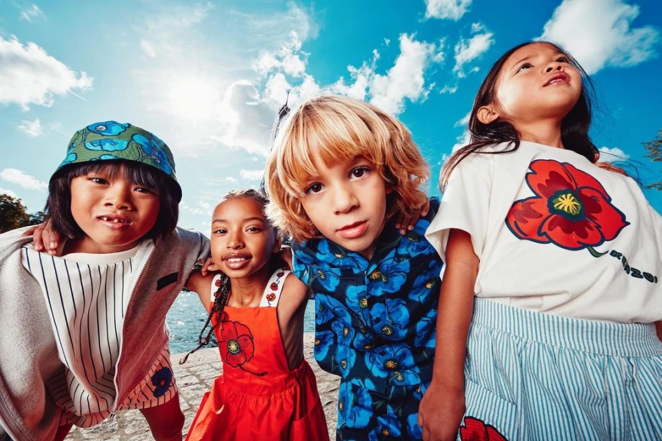 Four smiling children pose outdoors with a blue sky and the Eiffel Tower in the distance, showcasing vibrant floral-themed outfits.