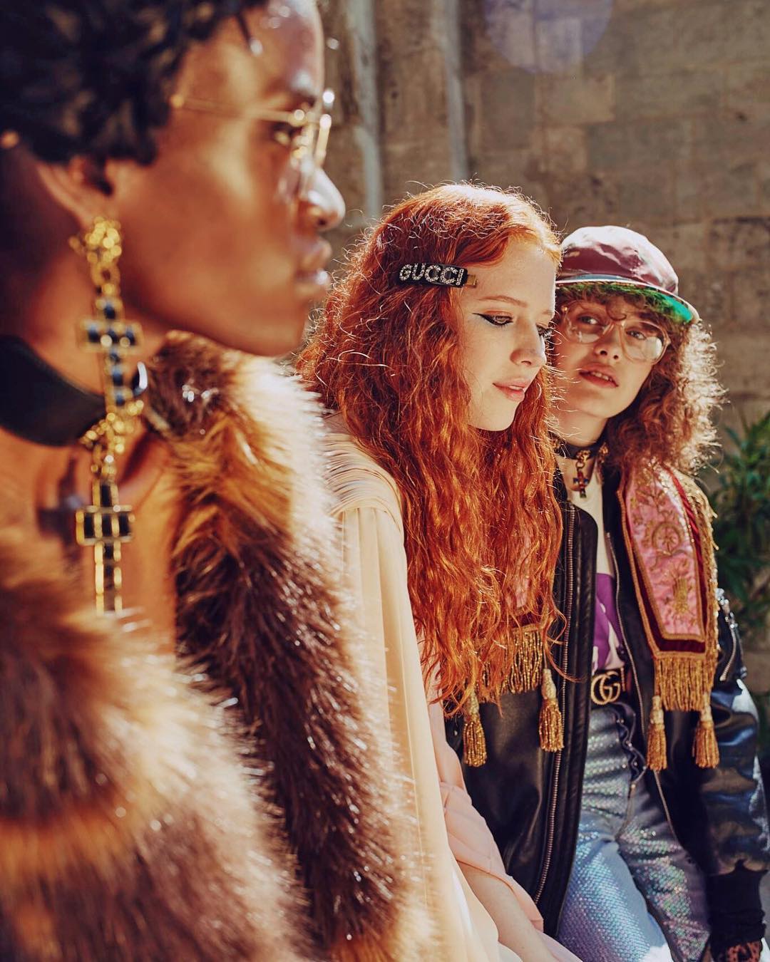 Three fashion models pose outdoors with retro-inspired styling, vintage-inspired apparel, and Gucci hair accessories, creating an editorial look.