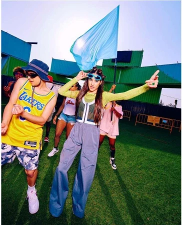 Group of young adults wearing casual clothing on a sunny day, with a large blue flag and green artificial turf.