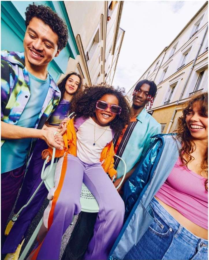 Group of five stylish young adults and a child posing on a city street with buildings in background. All are smiling.